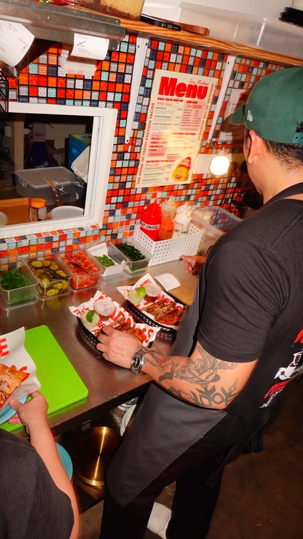 Chef Effardy finishing baskets of tacos at the pass under the Taco Madness menu